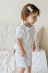 Toddler girl wearing the Avauma Mellow Days Set Vanilla Herb, standing on bed. Lightweight summer pajamas with delicate green floral pattern.